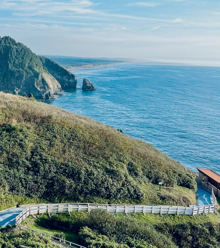 Green mountains meet the calm blue ocean and a winding road with white picket fence winds through them.