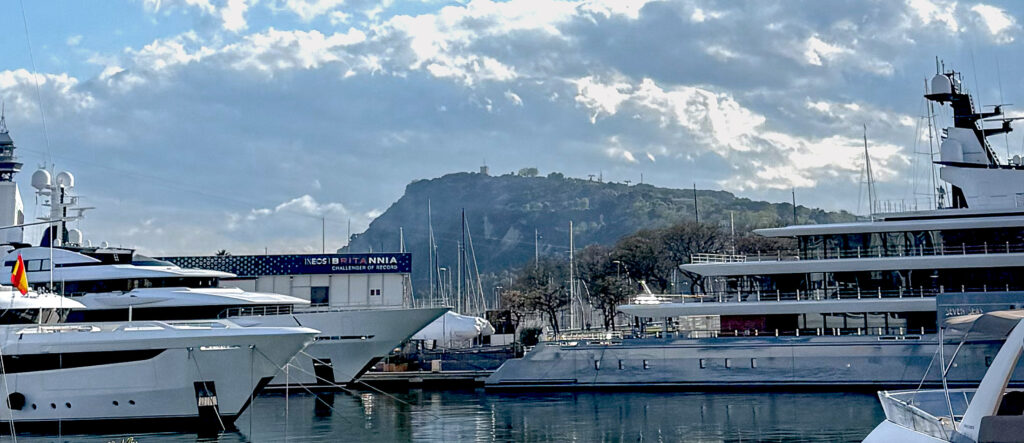 Closeup of several large yachts in the harbor with a distant mountain.