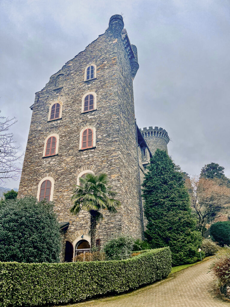 Ground view of an Italian Mediterranean European castle resort with tower. surrounded by trees, palm tree and manicured hedges.