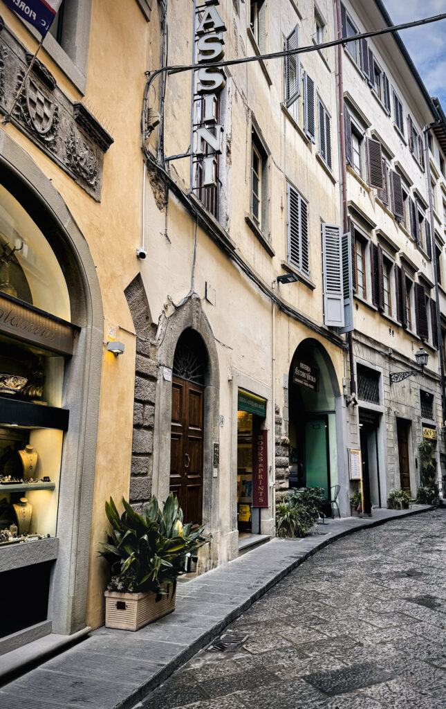 Romantic side perspective view of a European street with pale yellow buildings with arched doorways.