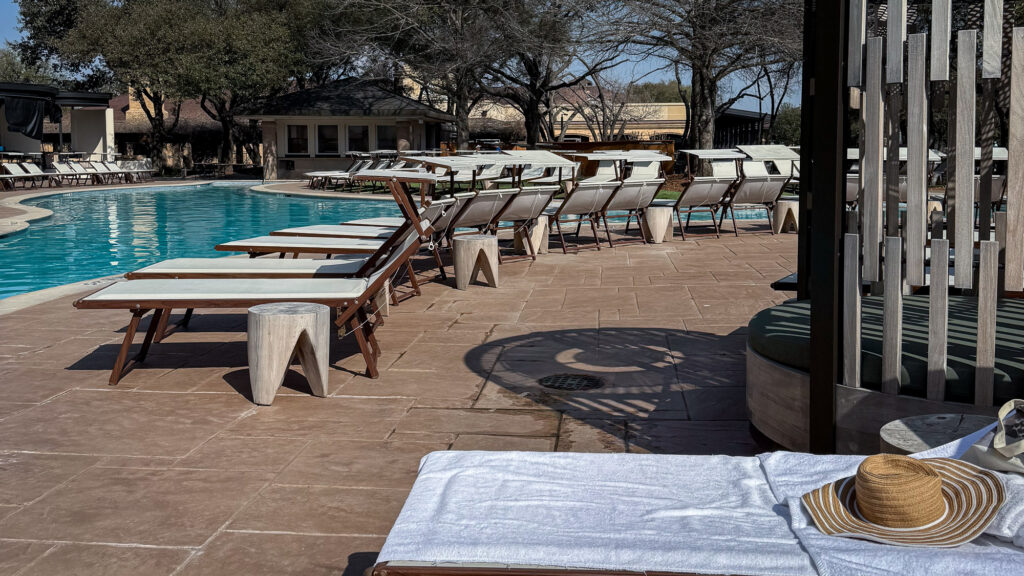 A straw hat sits on a beach chair near a cabana beside a resort pool
