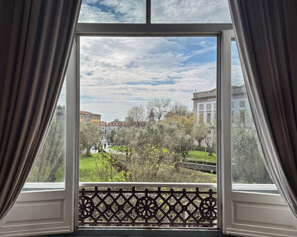 Balcony view through a curtained window to hotel grounds